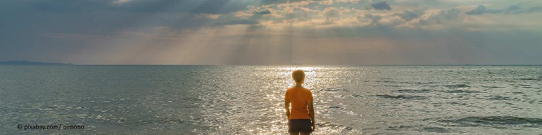 Frau mit Depressionen steht am Strand und blickt in dunkle Wolken mit Sonnenuntergang.