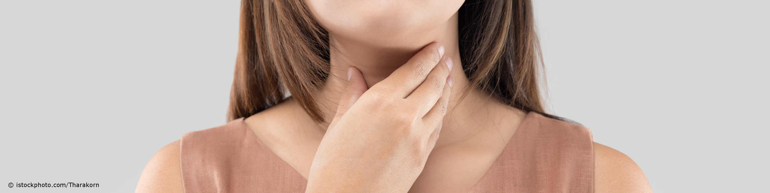 Frau mit Schilddrüsenunterfunktion tastet ihre Halsregion zwischen Adamsapfel und Schüsselbein ab.